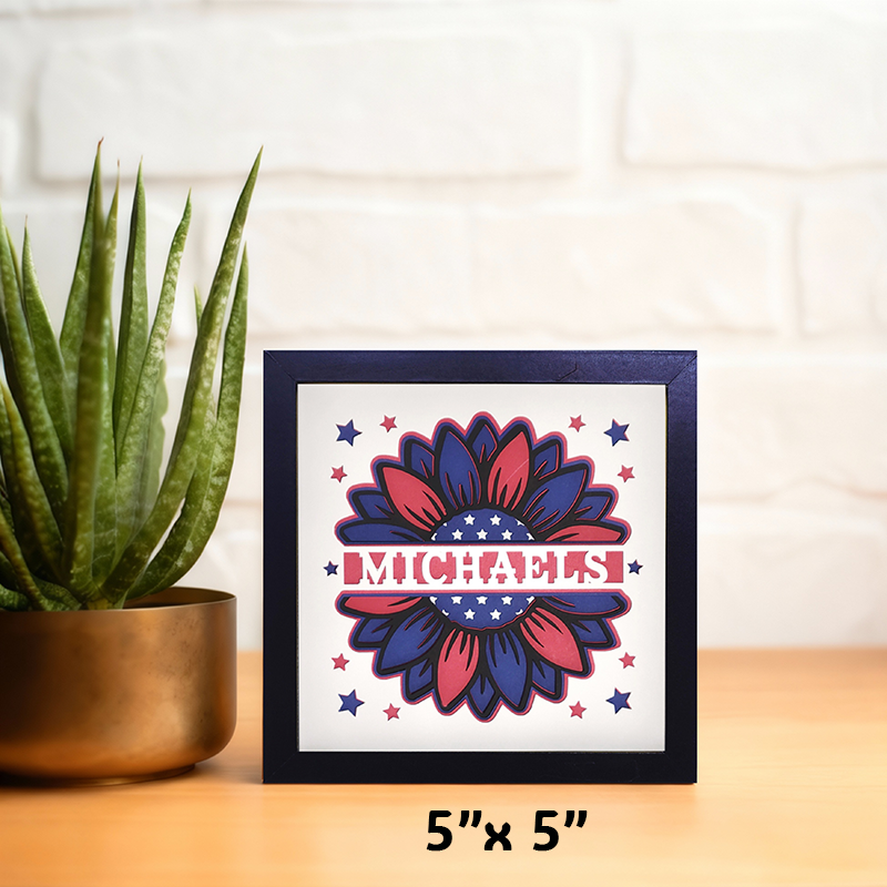 Framed artwork with a sunflower design and 'Michaels' text on a wooden surface with a plant.
