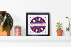Framed artwork with 'Welcome' text and floral design on a shelf with plants