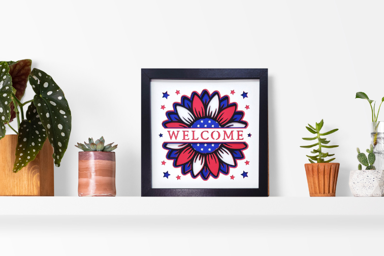 Framed artwork with 'Welcome' text and floral design on a shelf with plants