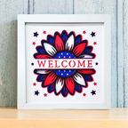 Framed artwork with a red, white, and blue floral design and 'WELCOME' text on a light wooden shelf.