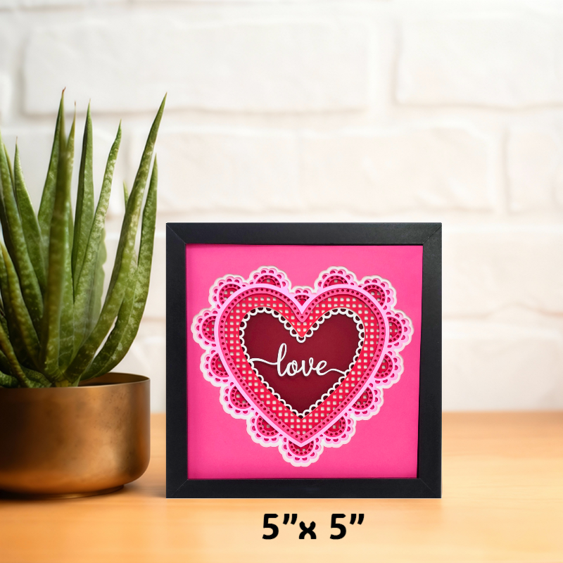 Framed heart-shaped artwork with 'love' text on a pink background, next to a plant.