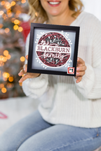 Person holding a framed family name sign with a blurred festive background