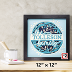 Framed artwork with 'the TOLLESON family' text on a light blue background, displayed on a desk.
