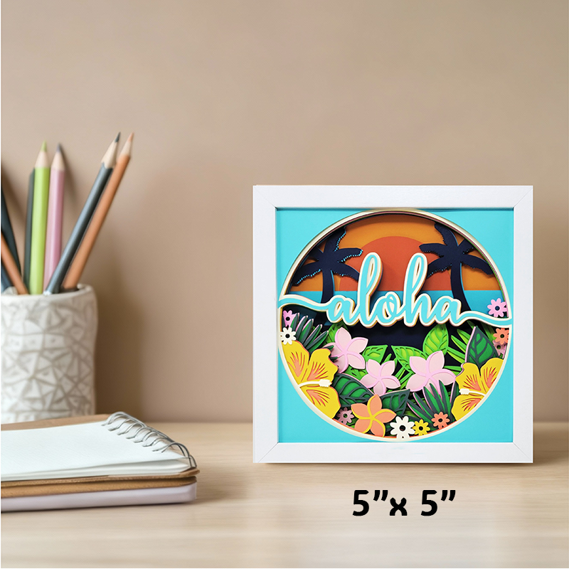 Framed decorative sign with 'aloha' text and tropical design on a desk with stationery items.