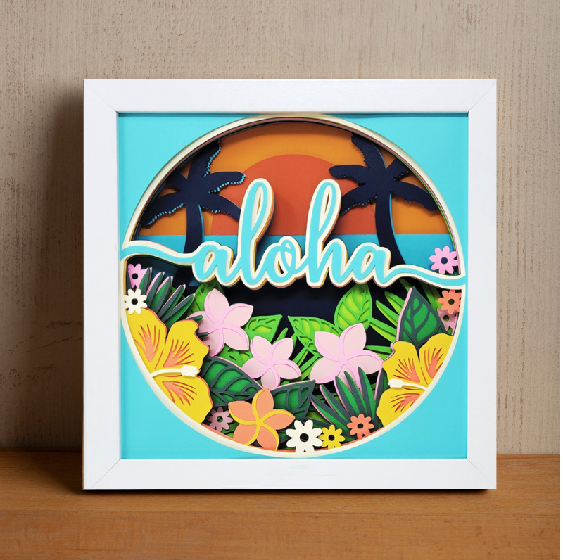 Framed artwork with 'aloha' text and tropical design on a wooden surface.