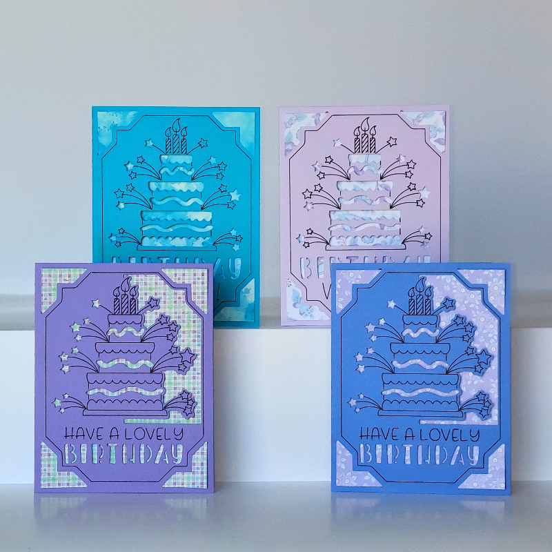 Four colorful birthday cards with cake designs on a white surface.