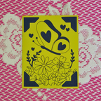 Yellow card with black floral and heart designs on a pink and white patterned background