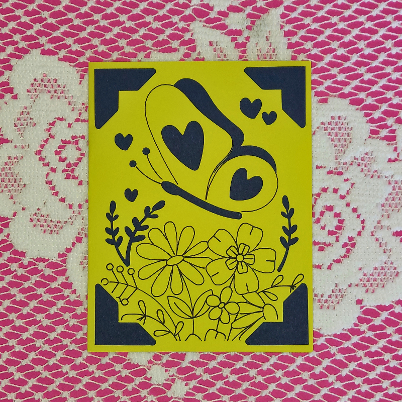 Yellow card with black floral and heart designs on a pink and white patterned background