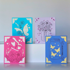 Four colorful greeting cards with floral, butterfly, and heart designs on a light gray background.