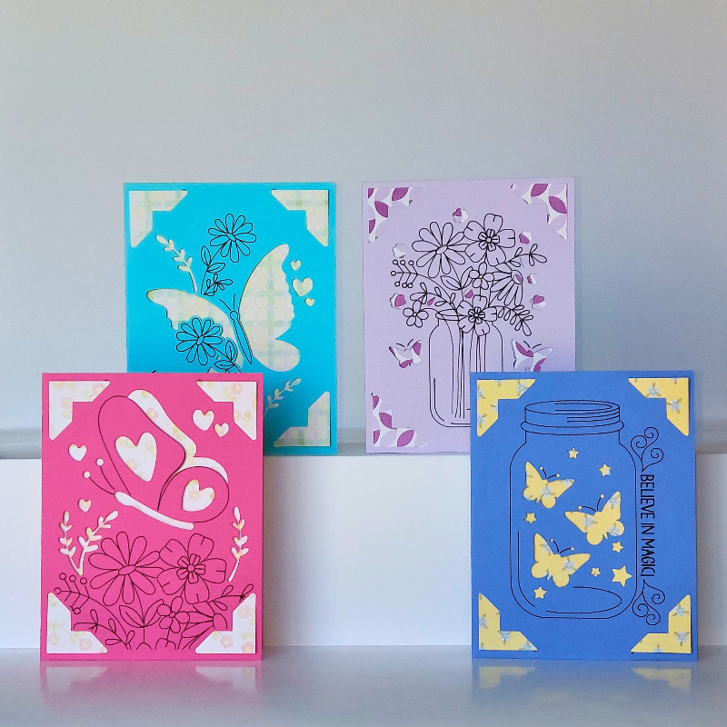 Four colorful greeting cards with floral, butterfly, and heart designs on a light gray background.