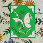 Green card with a pink butterfly design and 'WITH LOVE!' text on a floral fabric background.