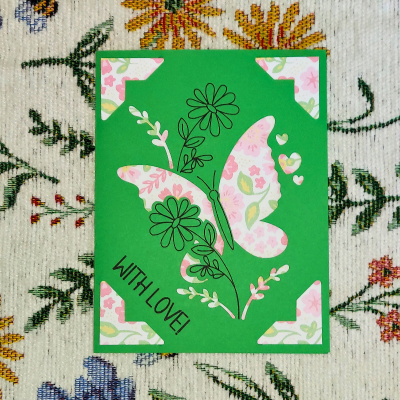 Green card with a pink butterfly design and 'WITH LOVE!' text on a floral fabric background.