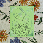 Green card with floral and snail design on a floral-patterned fabric background