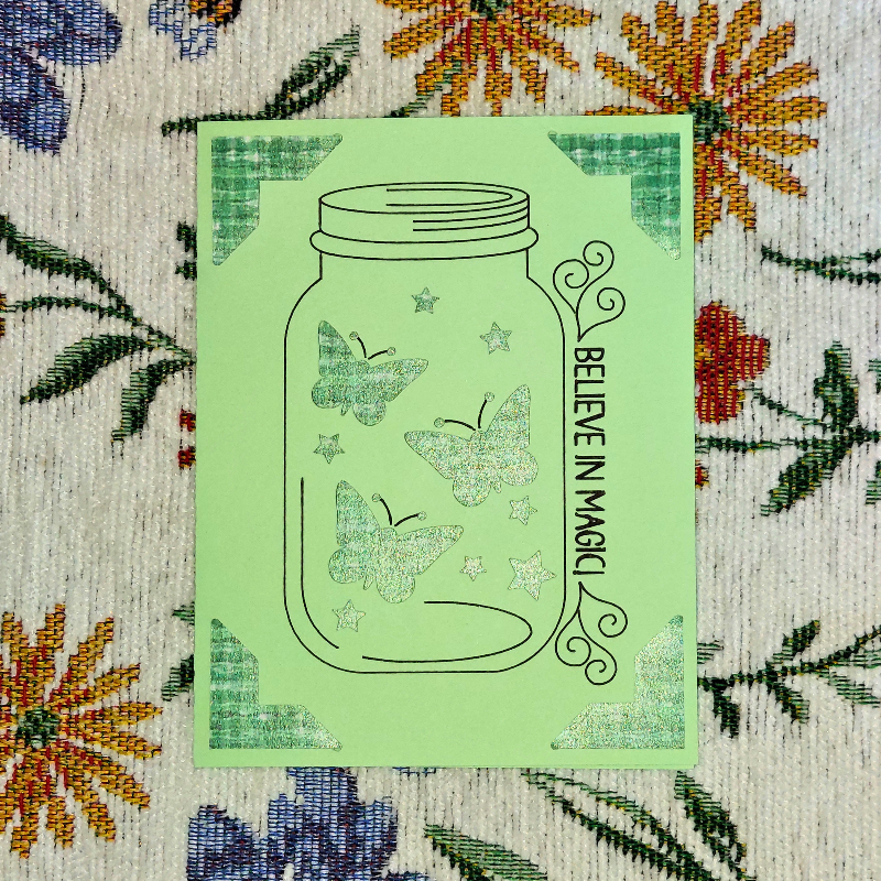 Green card with butterfly design and 'Believe in Magic' text on a floral background