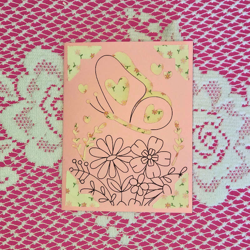 Card with floral and heart designs on a pink background, placed on a textured pink surface.
