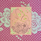 Card with floral and heart designs on a pink background, placed on a textured pink surface.