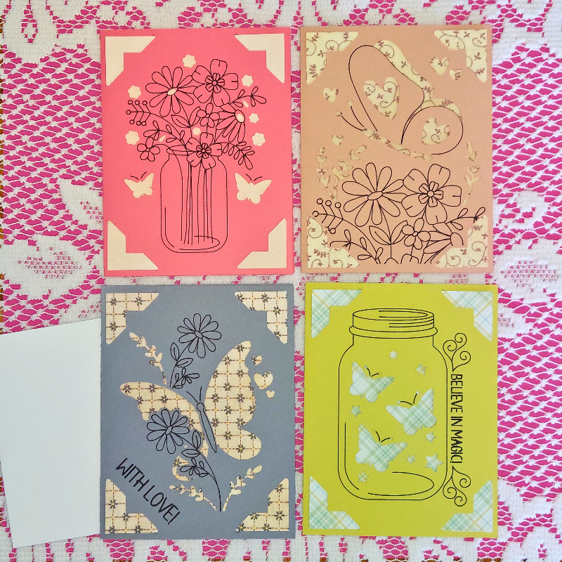 Four decorative cards with floral and butterfly designs on a lace background.