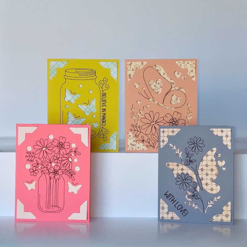 Four colorful greeting cards with floral and butterfly designs on a light blue background.