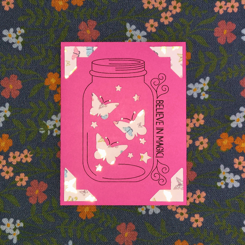 Pink card with butterfly design on a floral fabric background