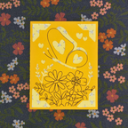 Yellow card with floral and heart designs on a dark fabric background with flowers.
