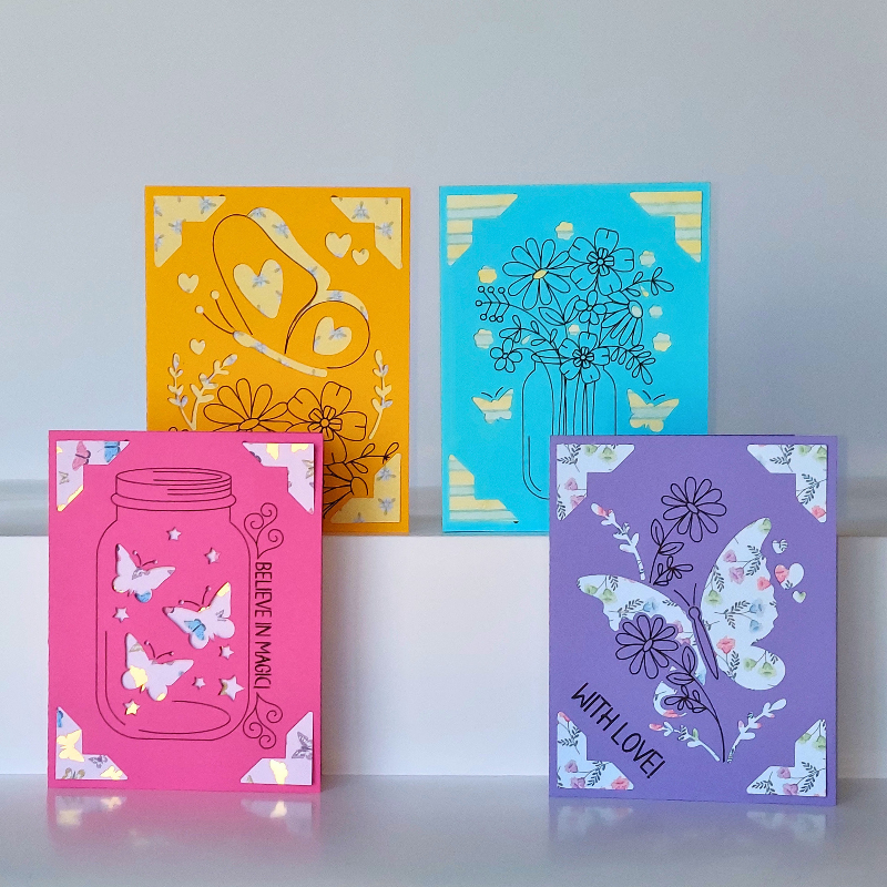 Four colorful greeting cards with floral and butterfly designs on a white surface.