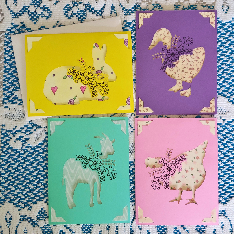 Four colorful greeting cards with animal illustrations on a patterned fabric background