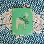 Card with a goat illustration on a green background, placed on a textured fabric surface.