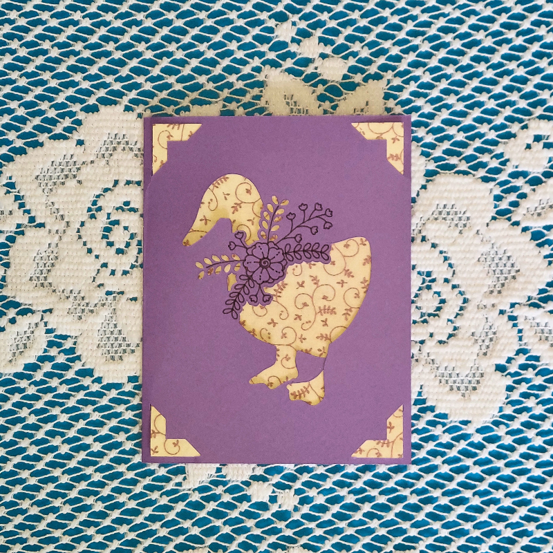 Purple card with gold goose design on a textured blue and white background