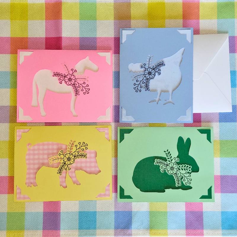 Four colorful greeting cards with animal illustrations on a checkered fabric background