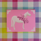 Card with a horse illustration on a pink background, placed on a colorful checkered fabric.