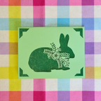 Green rabbit silhouette with floral details on a green square against a colorful checkered background
