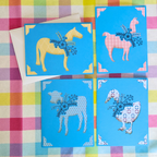 Four colorful greeting cards with animal illustrations on a checkered fabric background.