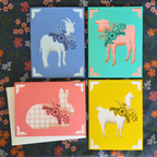 Four colorful greeting cards with animal illustrations on a floral background