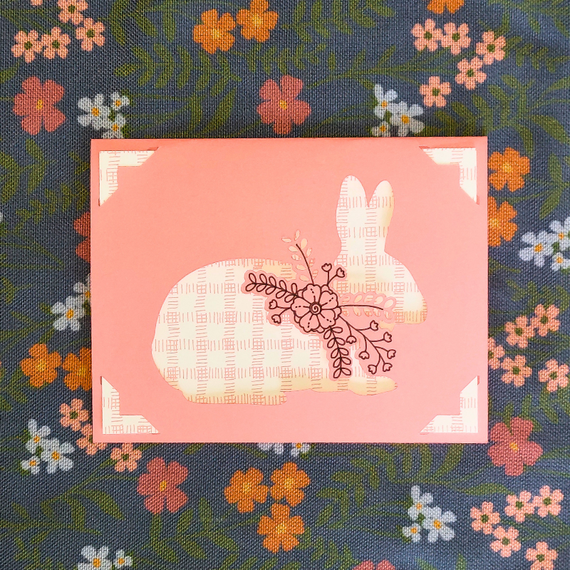 Decorative card with a bunny and floral design on a floral fabric background