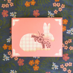 Decorative card with a bunny and floral design on a floral fabric background