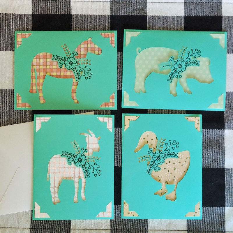 Four greeting cards with animal illustrations on a checkered fabric background