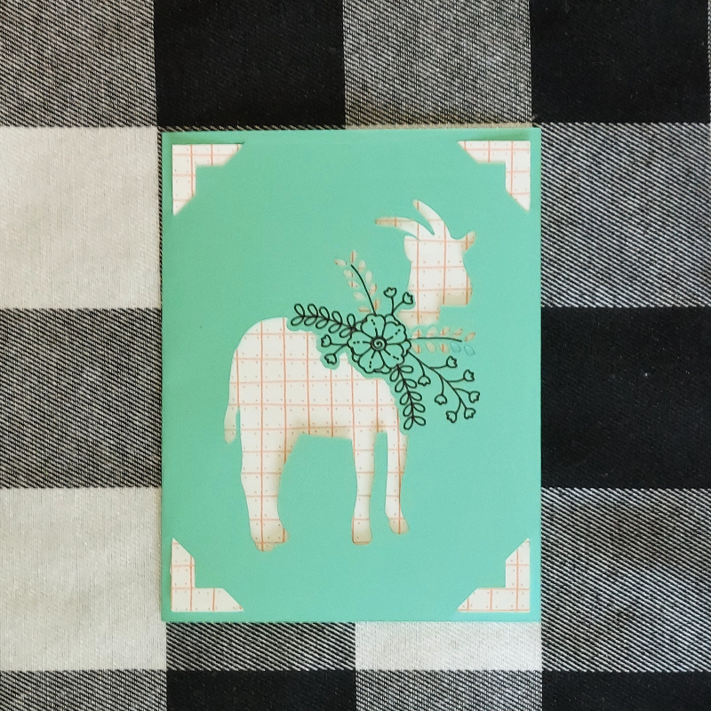 Card with a patterned goat design on a checkered fabric background