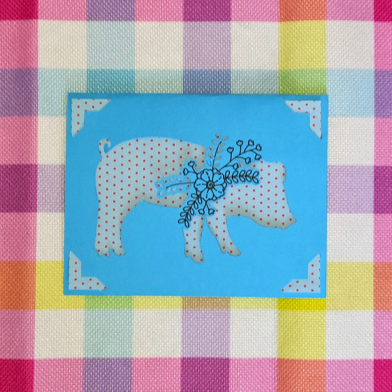 Decorative fabric with a checkered pattern and a central blue square featuring a polka dot pig design.