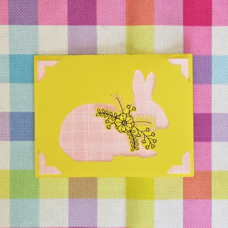 Card with a pink bunny and yellow flowers on a colorful checkered background