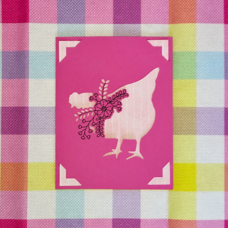 Card with a chicken design on a pink background, placed on a checkered fabric background.