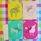 Four colorful greeting cards with animal illustrations on a checkered fabric background.