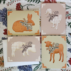 Four greeting cards with animal silhouettes and floral designs on a patterned fabric background.