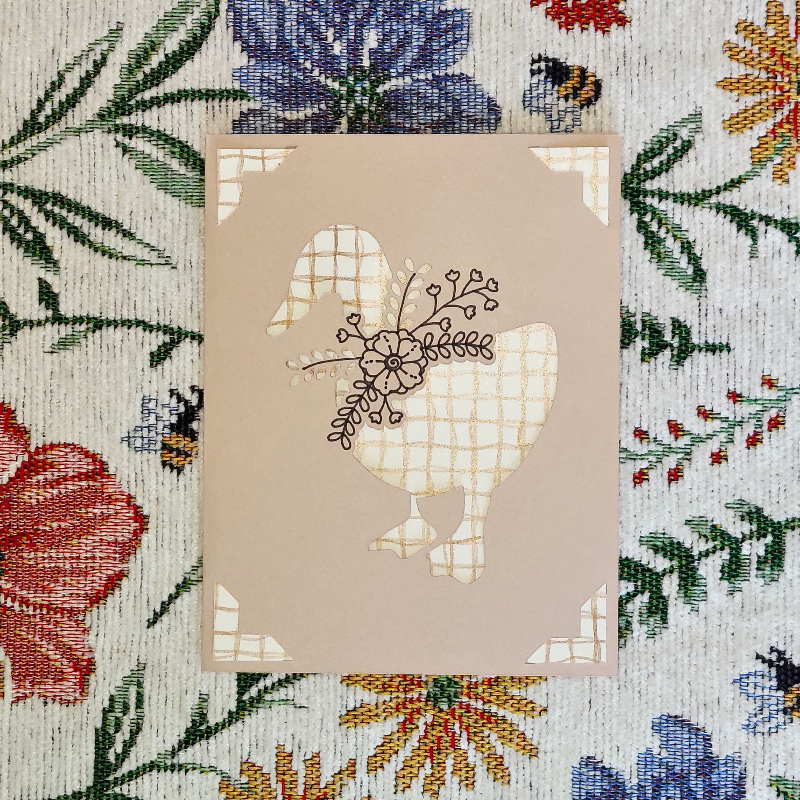Decorative card with goose design on a floral fabric background