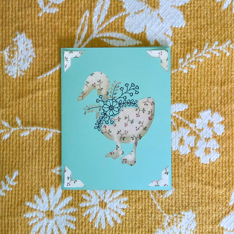 Card with a floral design on a duck on a textured yellow fabric background