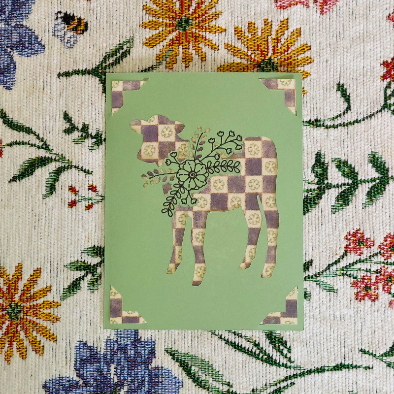 Patchwork cow design on a green card with floral background