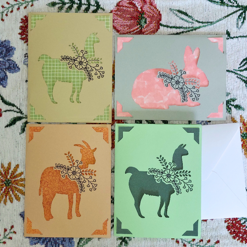 Four greeting cards with animal illustrations on a floral-patterned background