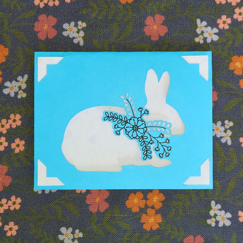 Fabric with a white rabbit holding a blue flower on a blue square, surrounded by floral patterns.