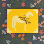 Decorative fabric with a yellow square featuring a white horse and floral design, on a floral-patterned background.