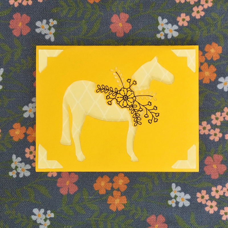 Decorative fabric with a yellow square featuring a white horse and floral design, on a floral-patterned background.