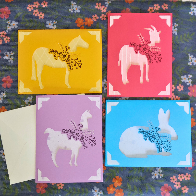 Four colorful greeting cards with animal illustrations on a floral background